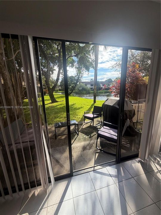 Sliding glass doors opening to a concrete patio with water frontage, lush lawn, and mature trees