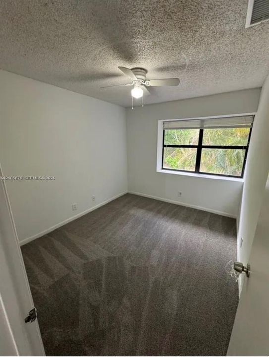 Neutral-toned carpeted flooring, white interior walls, ceiling fan with integrated lighting, and a multi-pane window with a horizontal blind