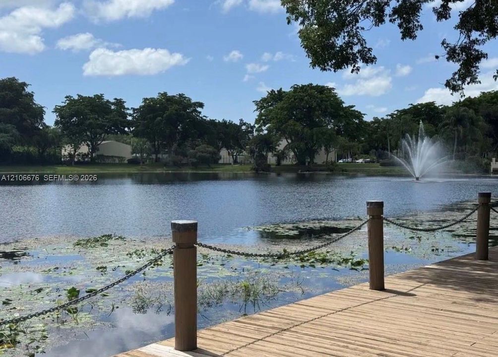 Wood-plank deck featuring posts with linked metal chain railings, overlooking a lake with a central fountain