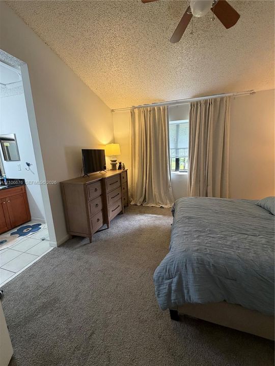 Vaulted ceiling with integrated wooden ceiling fan, neutral carpeting, and a vanity featuring a dark countertop