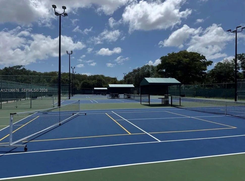 Multi-court tennis facility featuring hard-court surfaces, high-mast lighting, chain-link fencing, and covered spectator structures