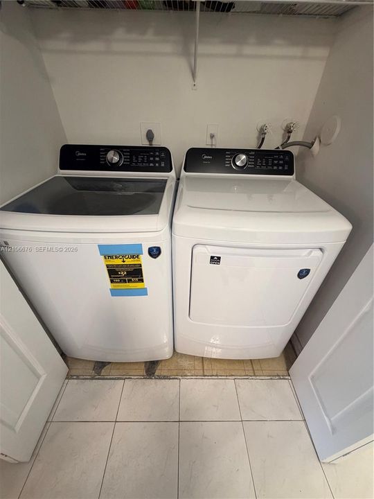 Dedicated laundry area featuring a white high-efficiency top-load washer and a matching white front-load electric dryer, set against white tile flooring