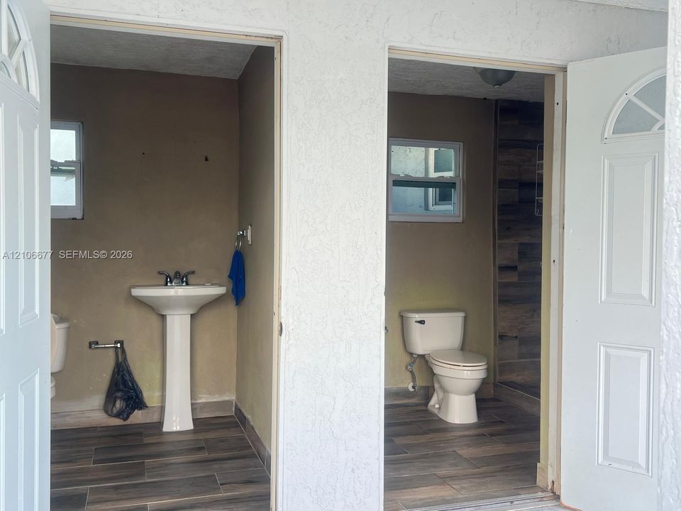 Dual entryways featuring white paneled doors, wood-finish flooring, a white pedestal sink, and a walk-in shower with wood-patterned tile surrounds