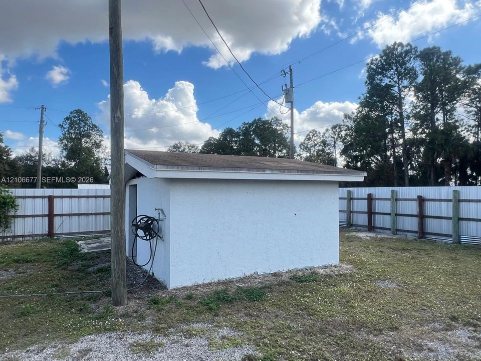 Detached structure featuring a stucco exterior, asphalt shingle roof, and metal perimeter fencing