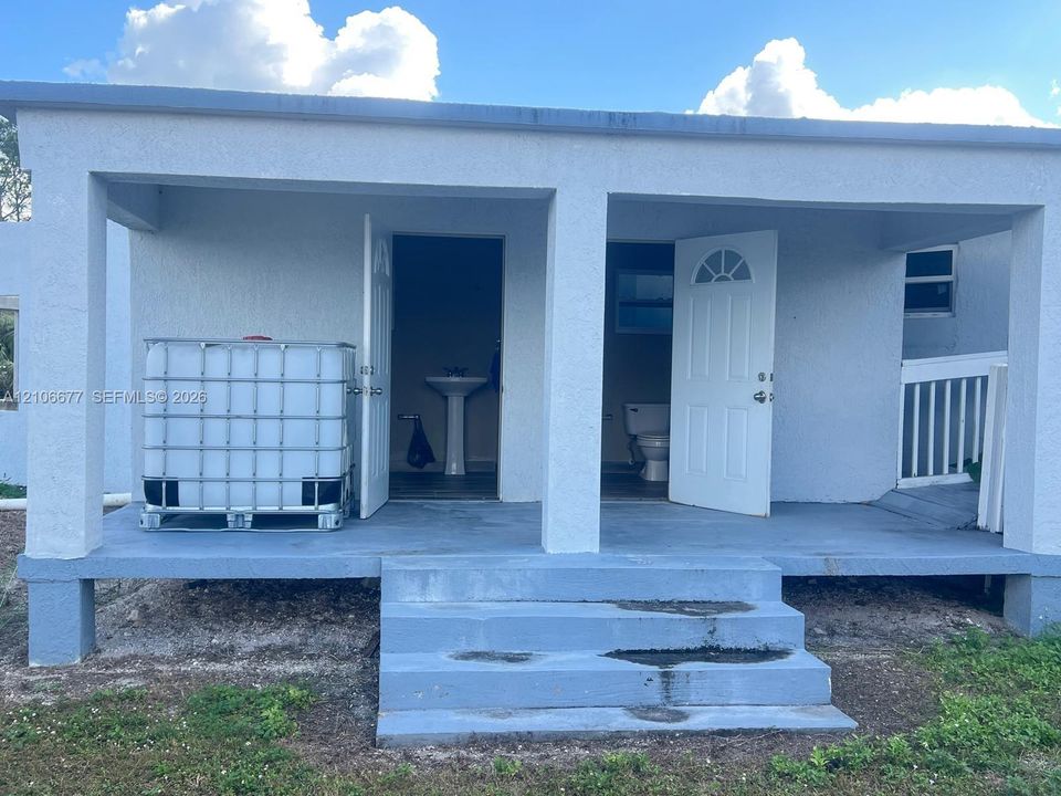 Covered porch featuring painted concrete flooring, masonry support pillars, concrete steps, and two entry points with arched-detail doors