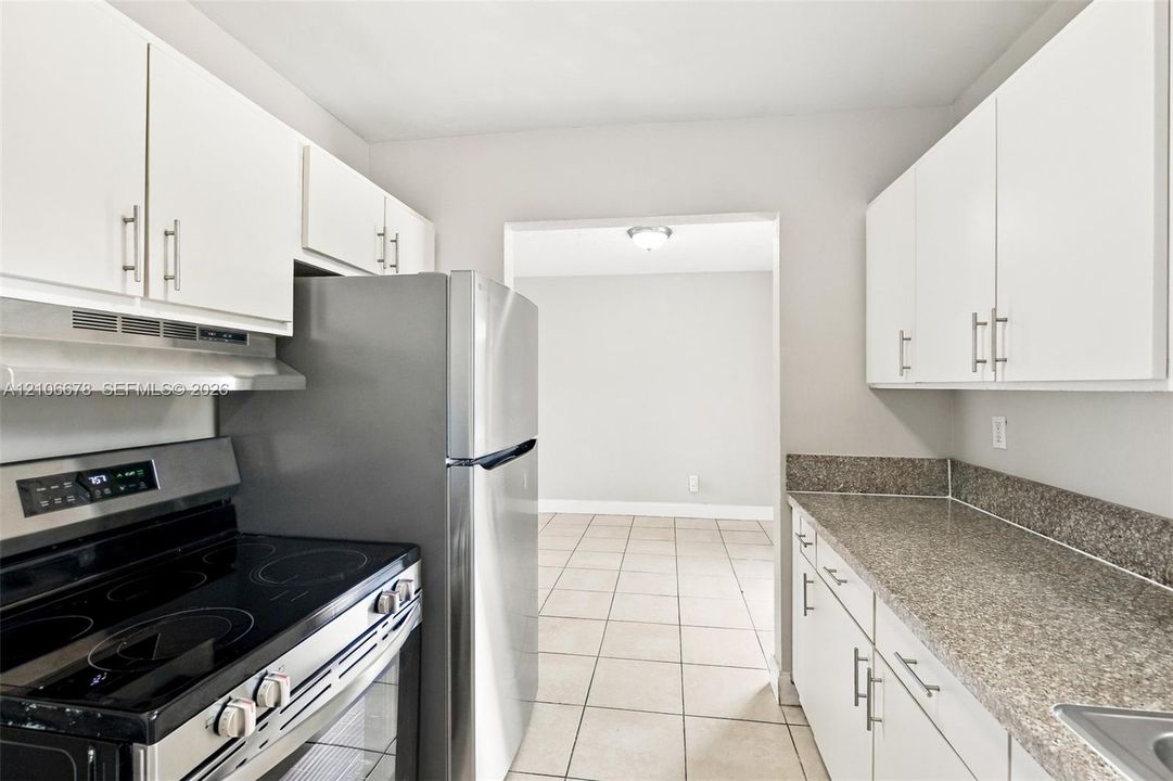Kitchen featuring white cabinetry with brushed metal hardware, speckled stone-finish countertops, stainless steel appliances, and neutral tile flooring
