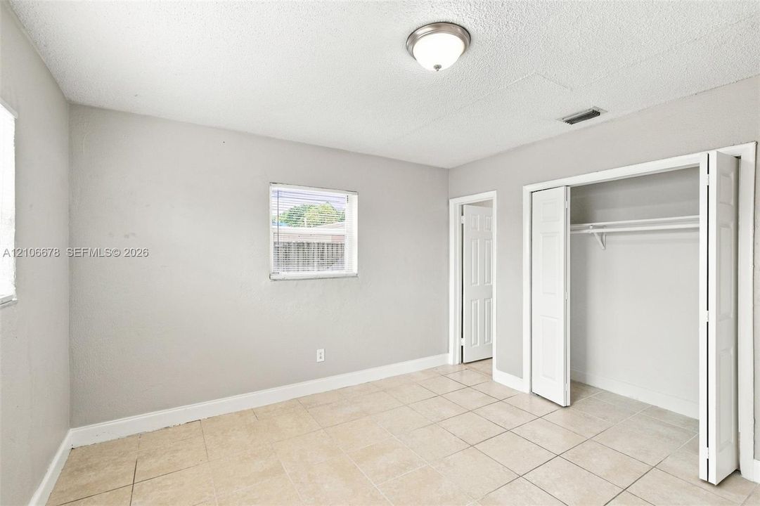 Neutral-toned room with tile flooring, dual-pane window, flush-mount ceiling light, and built-in closet with double-hinged doors