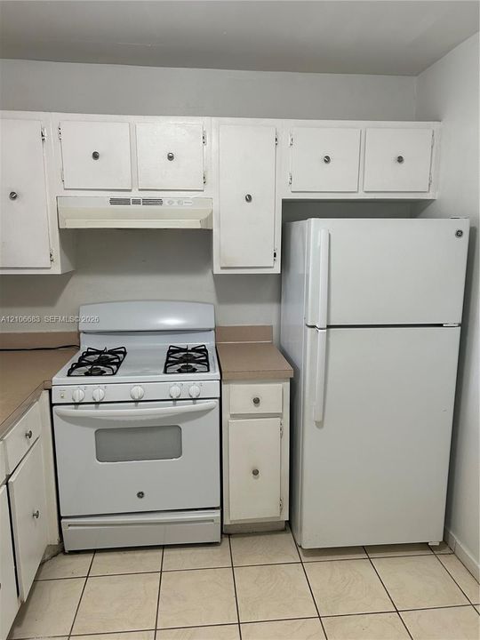 Kitchen featuring white cabinetry, gas range, integrated range hood, solid-surface countertops, and tile flooring