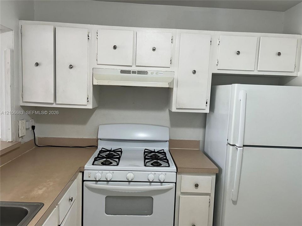 Kitchen featuring white cabinetry with circular hardware, neutral-toned countertops, a white gas range with an integrated hood, and a full-size white refrigerator