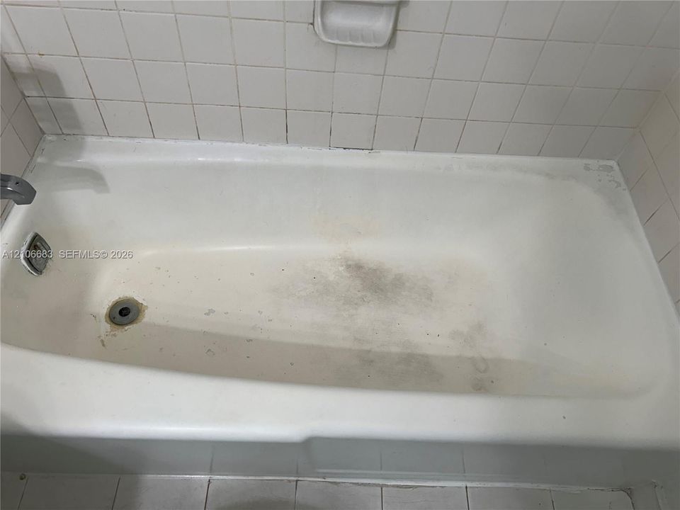 Bathtub with white square wall tile surround, integrated soap dish, and chrome-finish plumbing fixtures