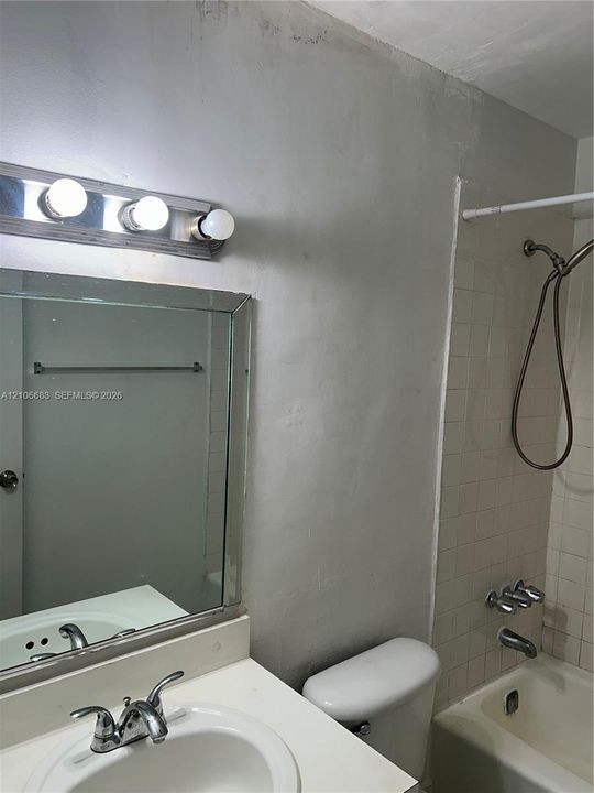Bathroom vanity with an integrated countertop sink, three-light wall-mounted fixture, rectangular mirror, and shower enclosure with tiled surround and handheld shower head