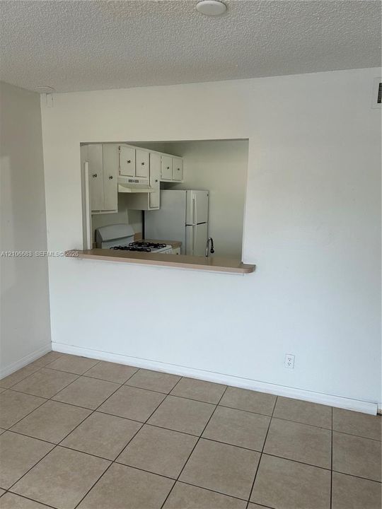 Kitchen features an open pass-through window with a built-in counter, white cabinetry, a white refrigerator, and a gas range, all finished with ceramic tile flooring