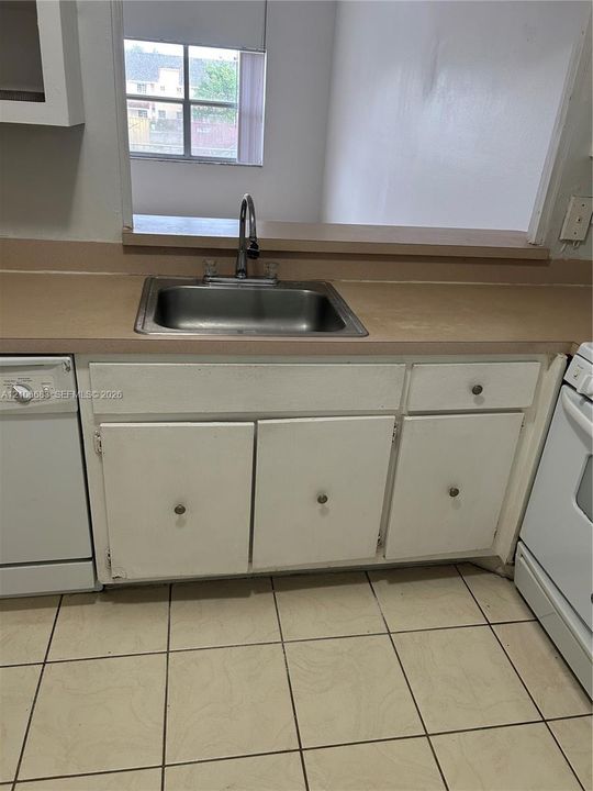 Kitchen area featuring white cabinetry, a neutral-toned countertop, a stainless steel undermount sink with a gooseneck faucet, and tiled flooring