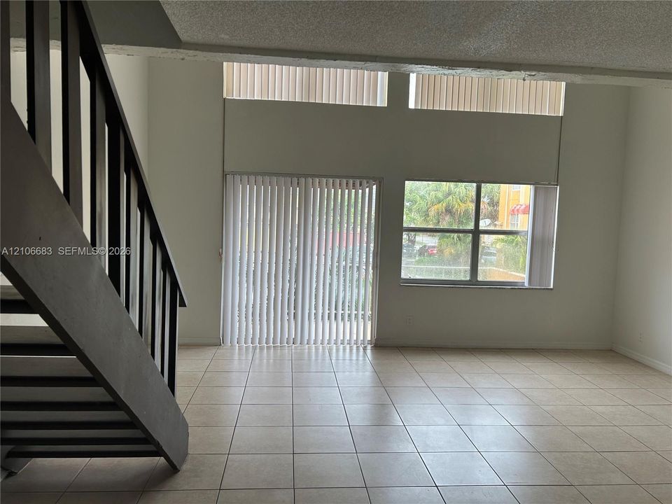 Open-concept room featuring high ceilings, ceramic tile flooring, vertical windows, a sliding glass door, and an open-riser staircase with a dark-finish railing
