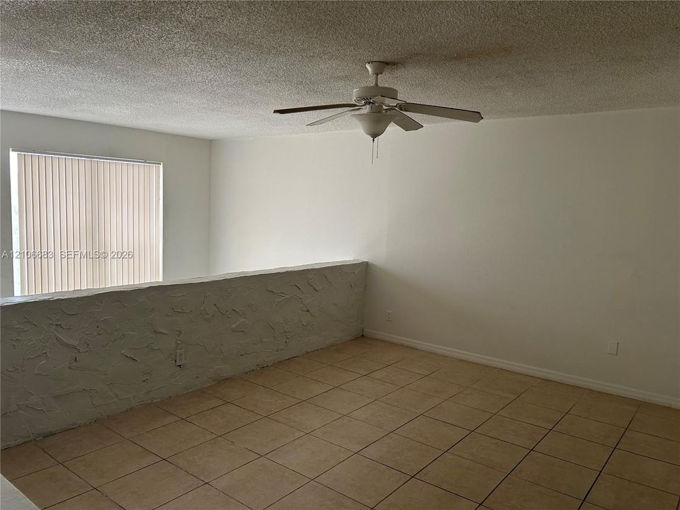 Room featuring ceramic tile flooring, textured half-wall detailing, vertical blinds, and a ceiling fan