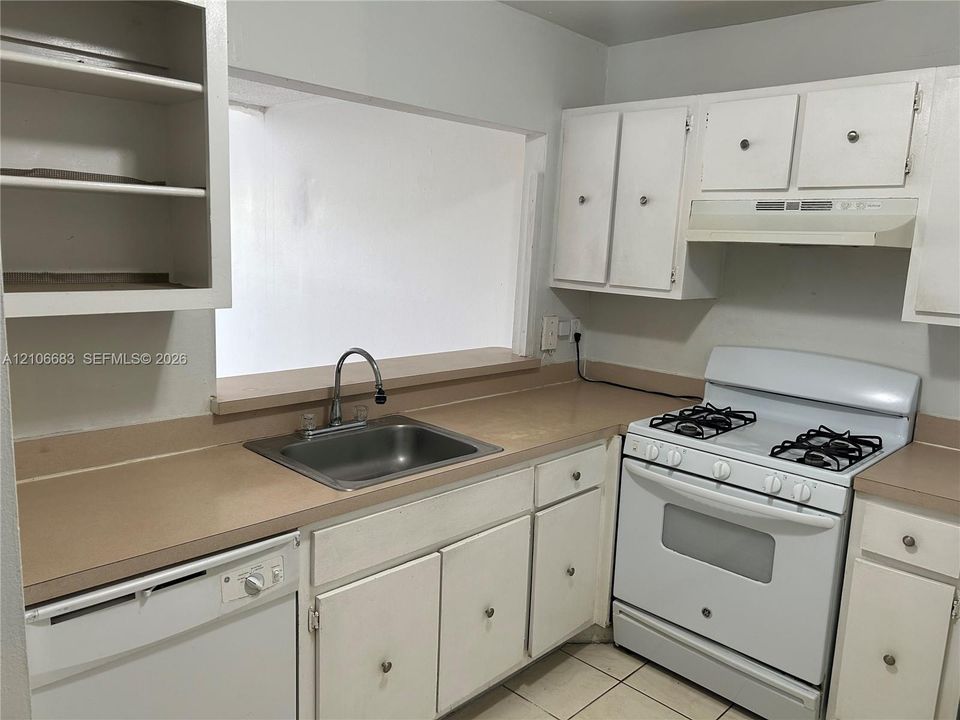 Kitchen featuring white cabinetry, solid-surface countertops, stainless steel sink with high-arch faucet, white dishwasher, and gas range