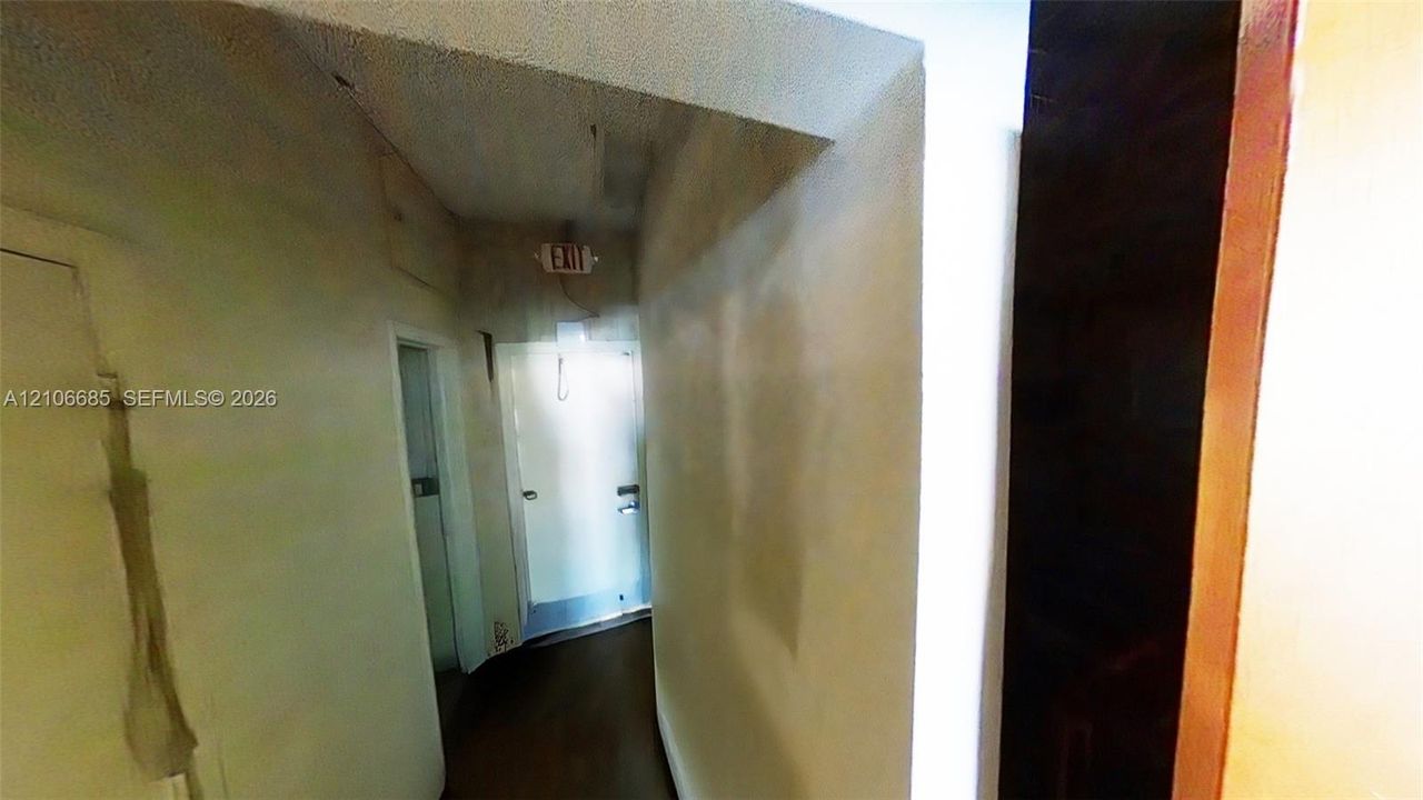 Interior hallway featuring white walls, wood-finish flooring, and a metal exit door