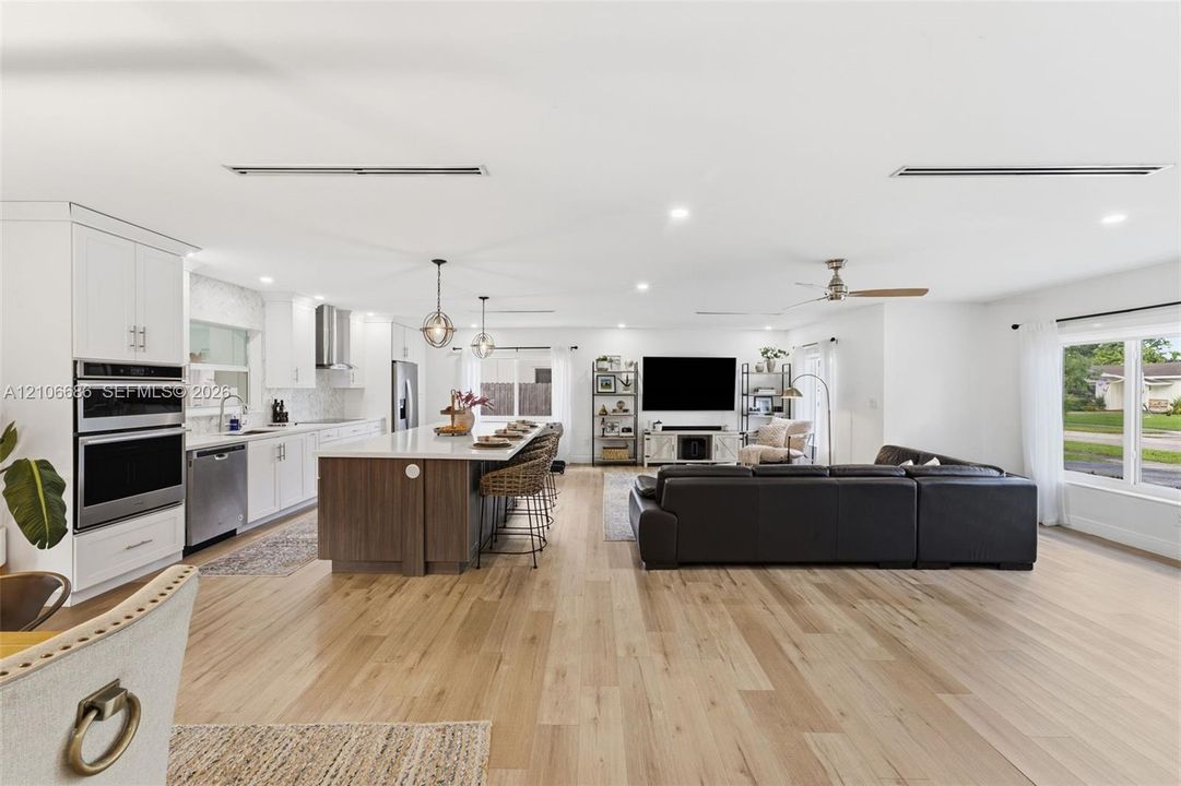Kitchen featuring a large center island with wood-finish cabinetry, stainless steel appliances including a built-in double oven, quartz countertops, and wood-finish flooring throughout