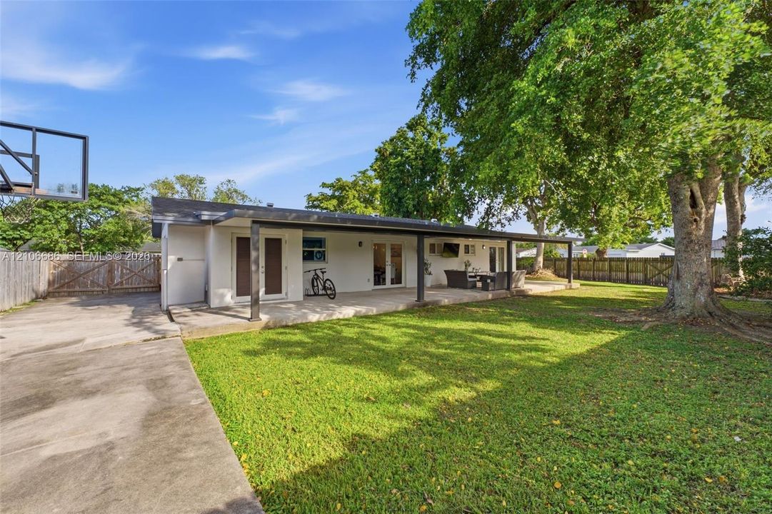 Expansive backyard featuring a covered patio, concrete surface, mature trees, and a wooden privacy fence