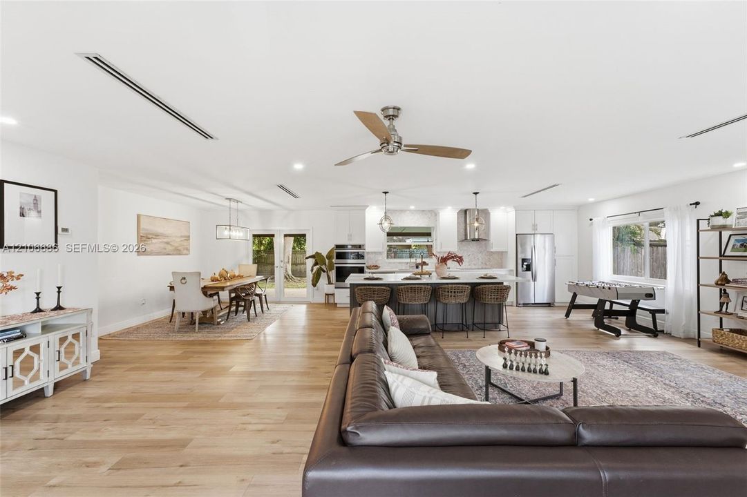 Open-concept interior featuring wood-finish flooring, recessed lighting, a central island with bar seating, integrated stainless steel appliances, and double-door glass exits