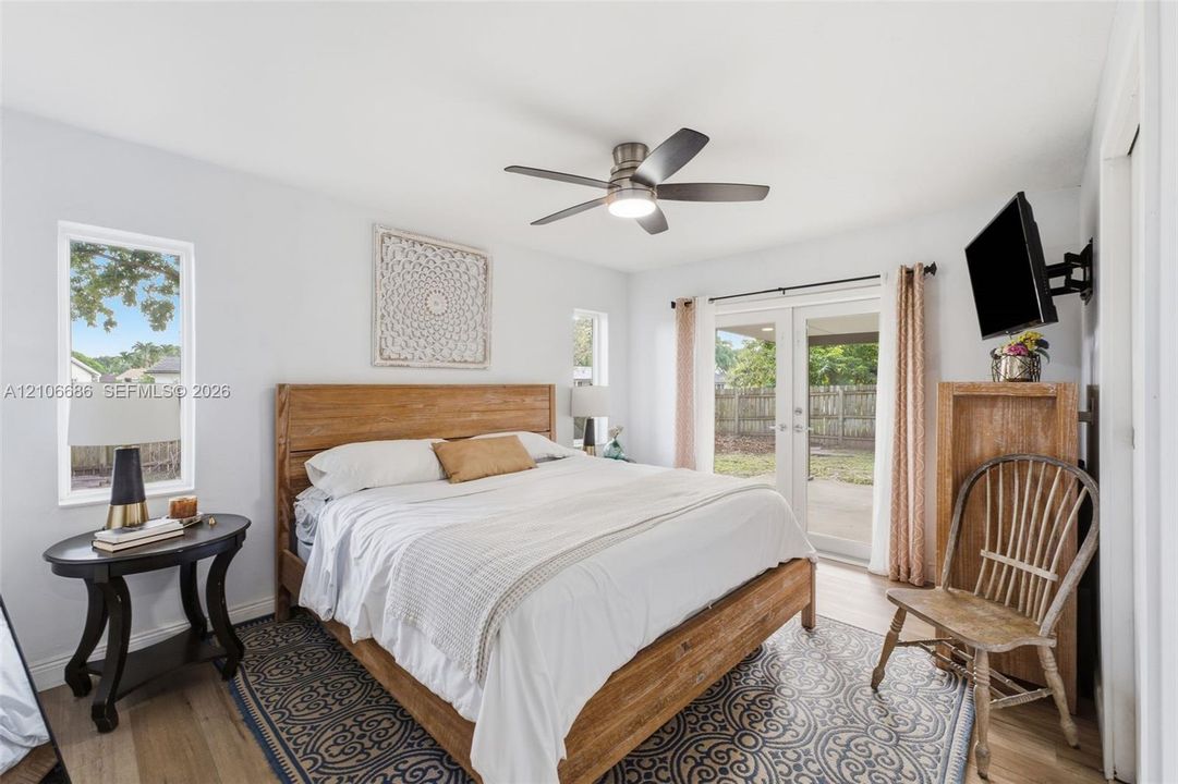 Room featuring wood-finish flooring, a ceiling fan with integrated lighting, and glass-paneled double doors providing outdoor access