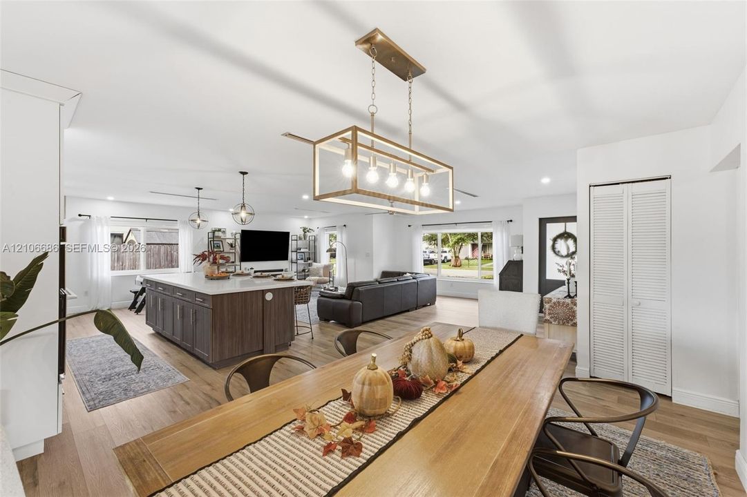 Open-concept area featuring wood-finish flooring, a kitchen island with stone countertop, rectangular linear pendant lighting, and louvered closet doors