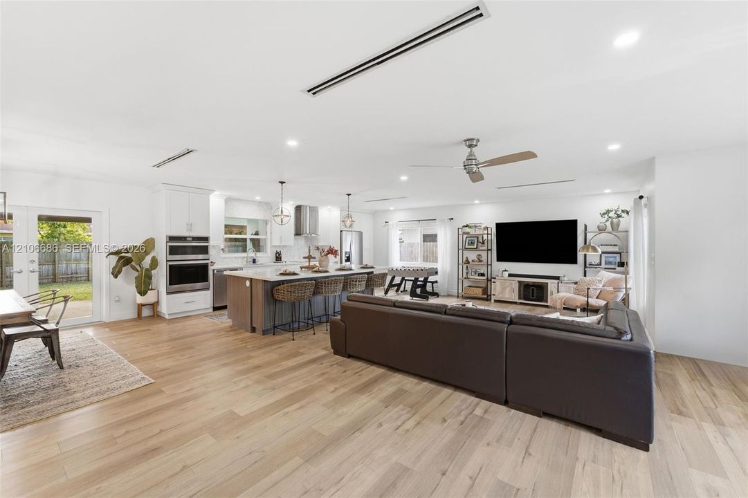 Open-concept interior featuring light wood-finish flooring, recessed lighting, double wall ovens, a kitchen island with bar seating, and double glass-paned doors