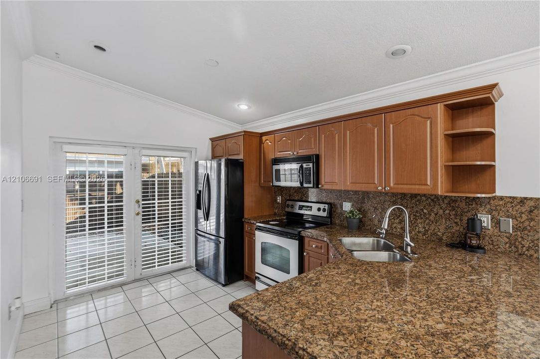 Kitchen featuring solid-surface countertops, wood-finish cabinetry, stainless steel appliances, ceramic tile flooring, and glass-paned double doors
