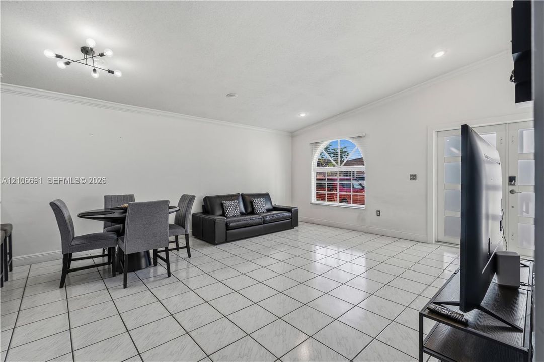 Open-concept interior featuring light-toned tile flooring, vaulted ceilings, a prominent arched window, recessed lighting, and a multi-light chandelier
