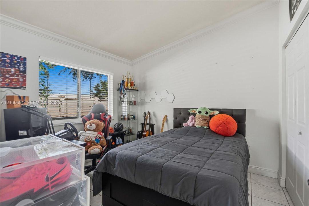 Room featuring light-toned tile flooring, neutral wall paint, white crown molding, a multi-pane horizontal window, and a white six-panel closet door