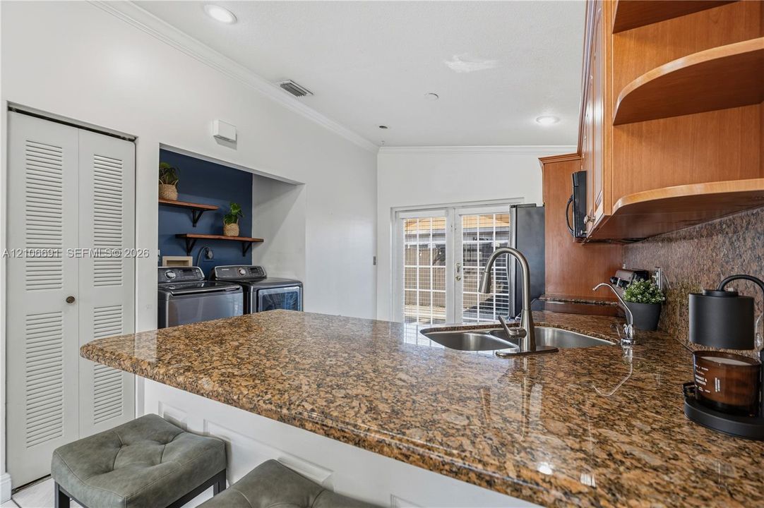 Kitchen featuring a stone-surface breakfast bar, wood cabinetry, recessed lighting, and a dedicated laundry area with built-in shelving