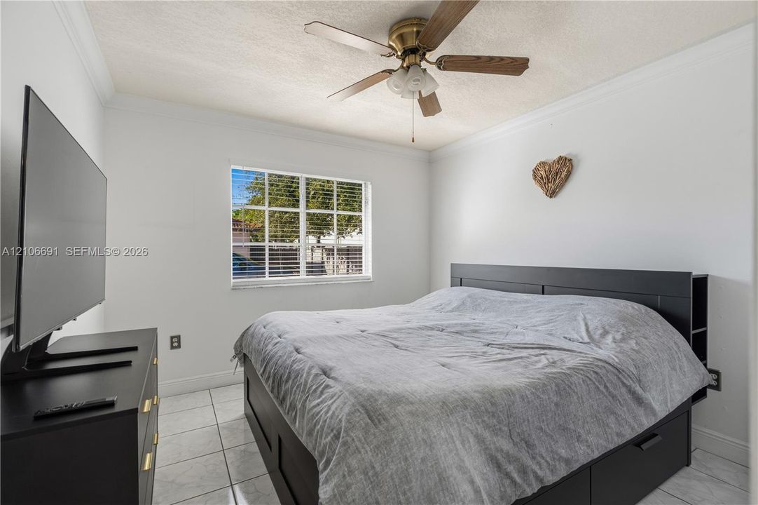 Neutral-toned room featuring a multi-pane window, tile flooring, and a ceiling-mounted fan with integrated lighting