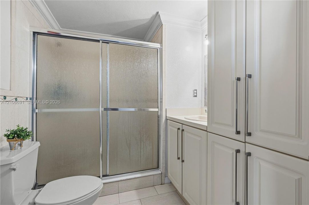 Bathroom featuring a glass-enclosed shower, expansive floor-to-ceiling cabinetry, neutral tile flooring, and integrated countertop vanity