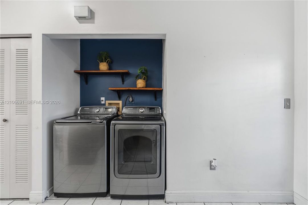 Laundry area featuring stainless steel appliances, dual wall-mounted natural wood shelving, and tiled flooring