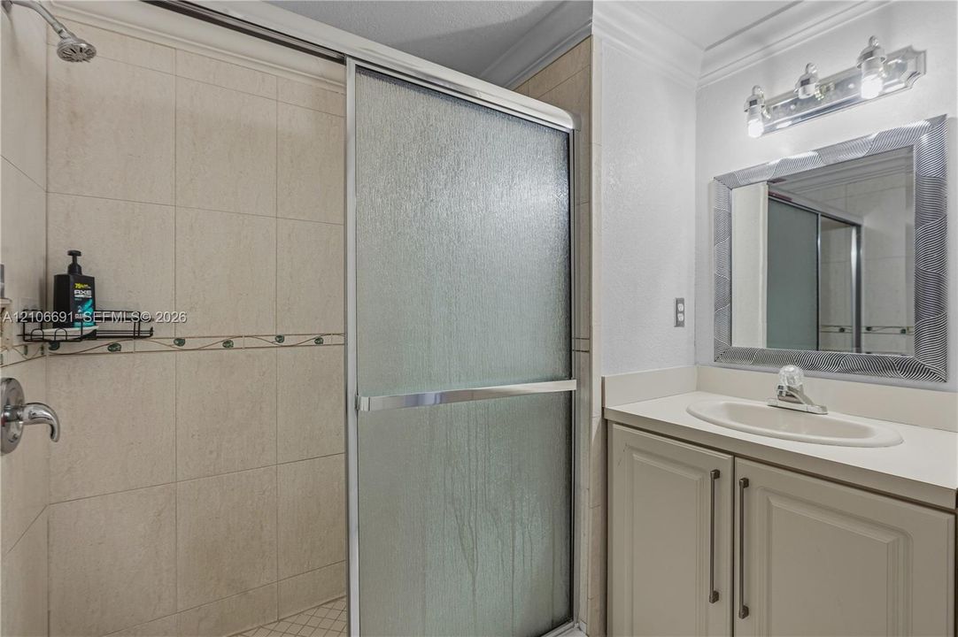 Bathroom featuring a vanity with integrated sink, chrome faucet, wall-mounted vanity lighting, mirror with a decorative frame, and a tiled shower enclosure with sliding glass doors
