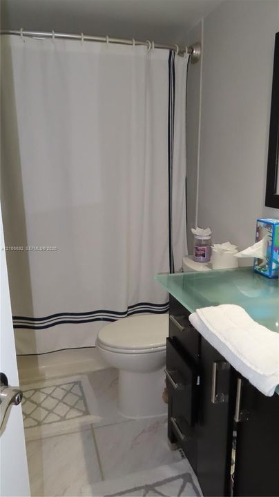 Bathroom featuring dark cabinetry with brushed metal hardware, a frosted glass countertop, and tiled flooring