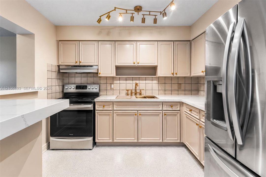 Kitchen featuring custom-color cabinetry, stainless steel appliances, stone-surface countertops, square-tiled backsplash, and multi-directional track lighting