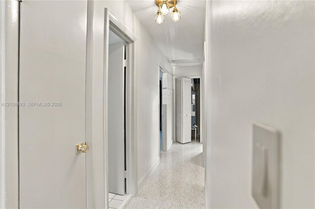 Hallway featuring neutral wall finishes, terrazzo flooring, and a multi-bulb ceiling-mounted light fixture