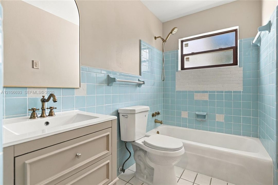 Bathroom featuring blue tile wainscoting, vanity with integrated sink, brass-finish faucet and shower fixtures, arched wall mirror, and bathtub with tile surround