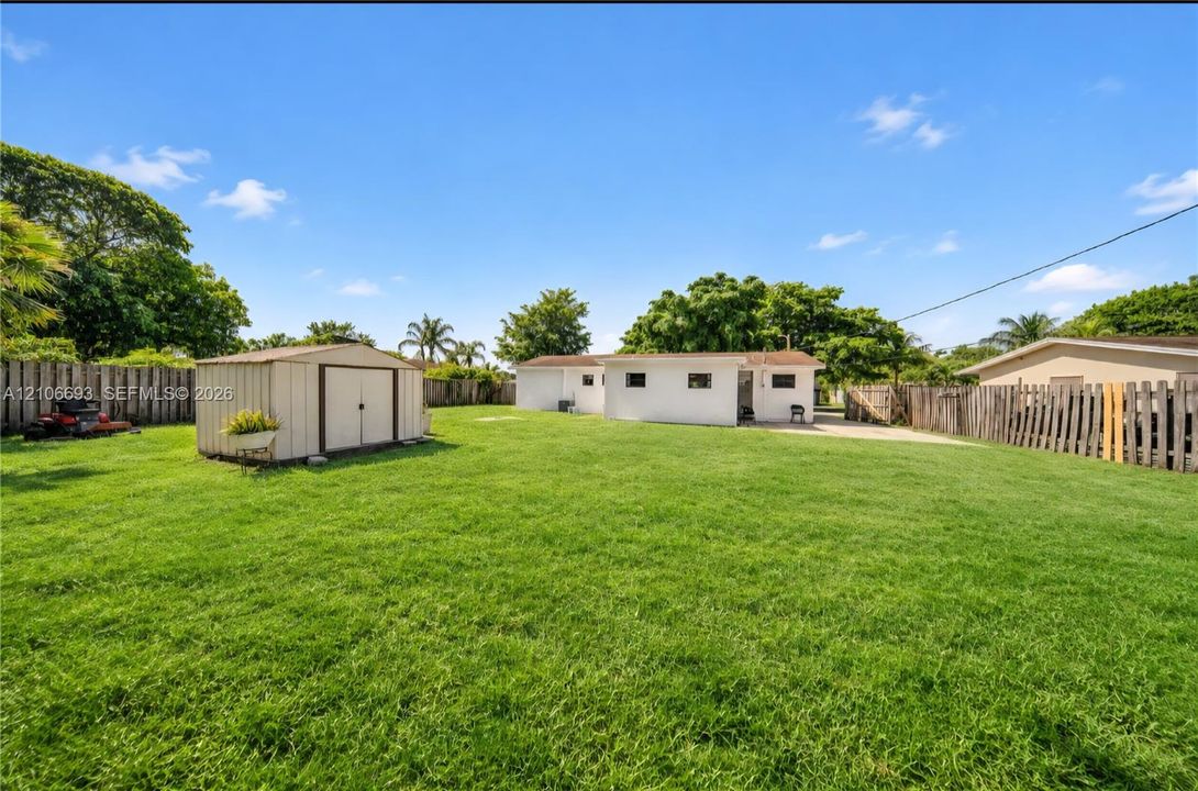 Expansive backyard featuring a large grass lawn, perimeter wood fencing, and a detached storage shed