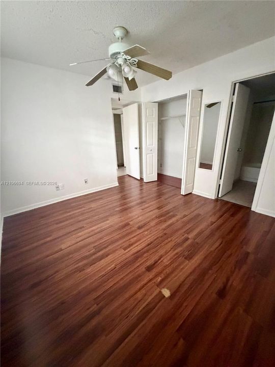 Wood-finish flooring, ceiling fan with integrated lighting, bi-fold closet doors, and recessed mirror panel