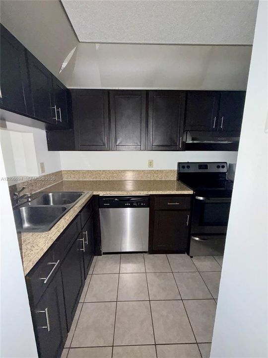 Kitchen featuring dark-toned cabinetry, stone-finish countertops, tile flooring, stainless steel dishwasher, and dual-basin sink