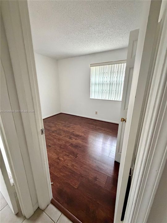 Room featuring wood-finish flooring, white walls, and a window with vertical blinds