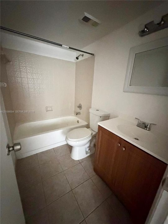 Bathroom featuring tile flooring, a tub and shower combination with tiled surround, a wood-finish vanity with an integrated sink, and a framed wall-mounted mirror