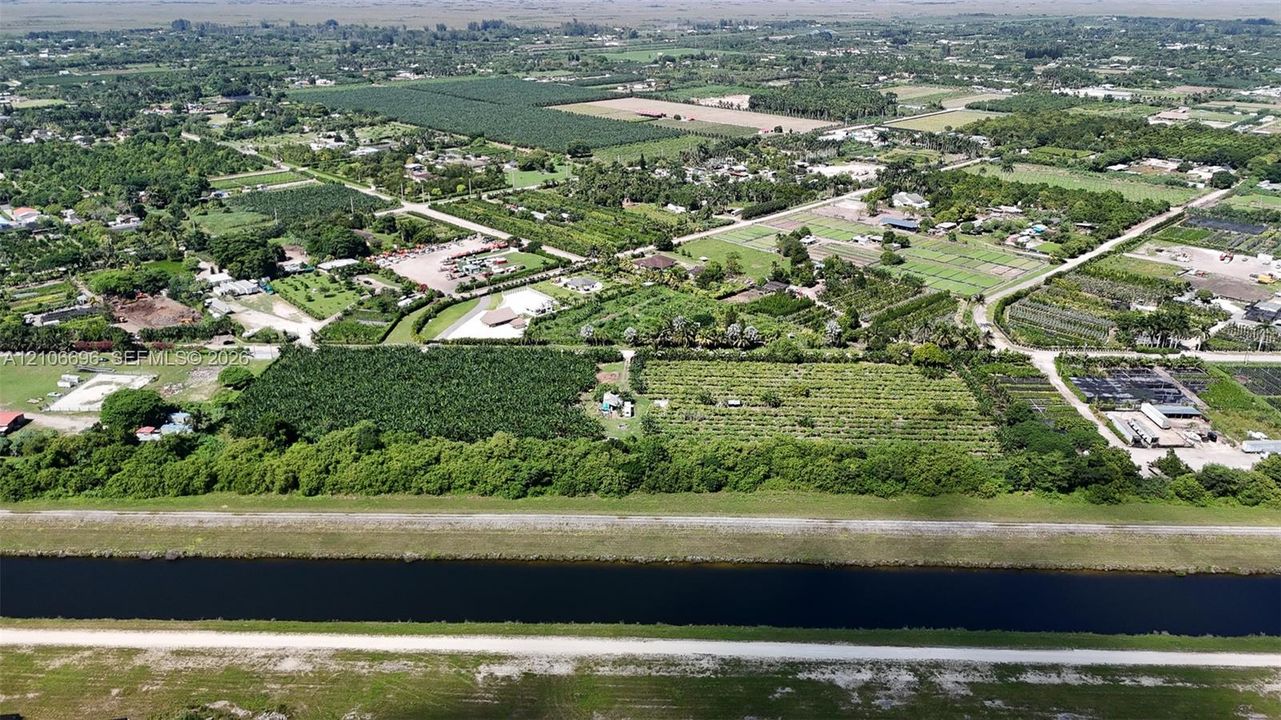 Aerial perspective featuring expansive agricultural acreage, mature perimeter landscaping, and frontage along a water canal