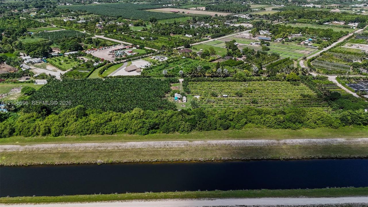 Aerial perspective of expansive acreage featuring mature agricultural plantings, a cleared central building site, and direct canal frontage