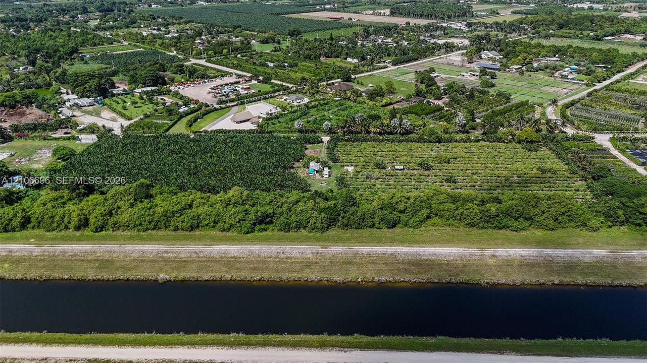 Aerial perspective featuring extensive agricultural acreage, dense mature vegetation, and direct canal frontage