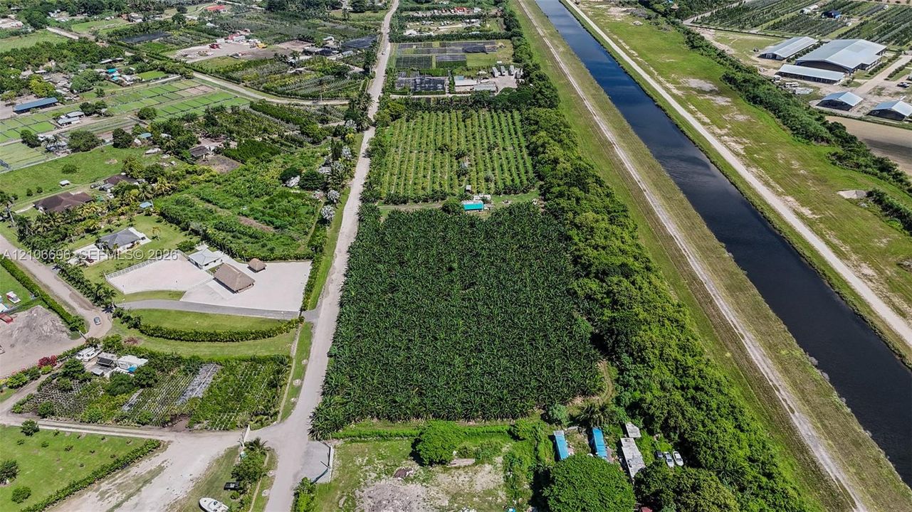 Aerial perspective of a sprawling land parcel featuring extensive agricultural acreage, mature tree canopy, and proximity to a canal