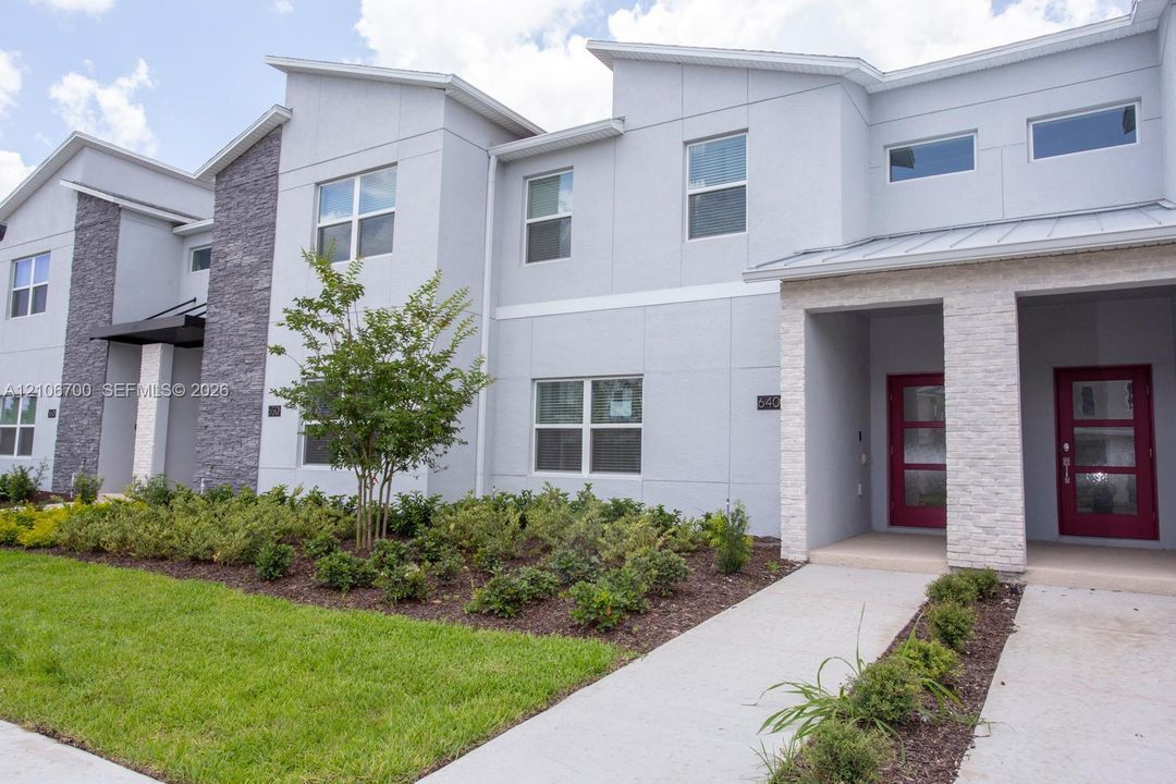 Contemporary exterior featuring multi-textured facade with grey paneling and stone veneer accents, shed-style rooflines, and bold red-toned front entry doors