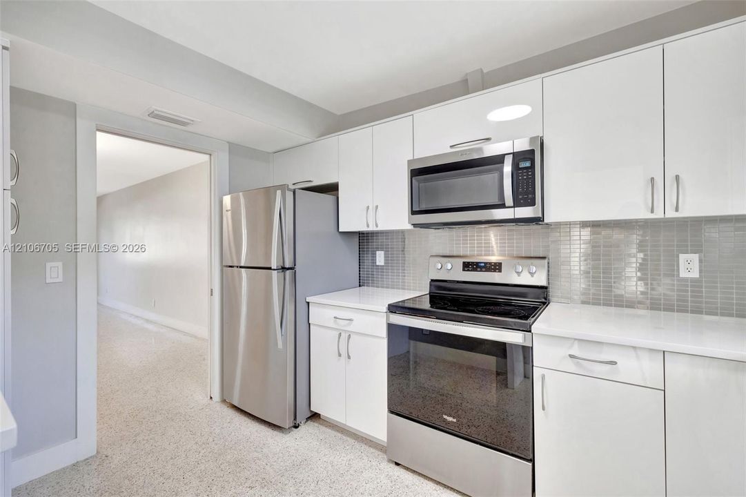 Kitchen featuring white cabinetry, solid-surface countertops, mosaic tile backsplash, and stainless steel appliances including a refrigerator, over-the-range microwave, and electric range